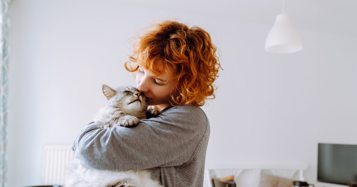 A lady in a white top hugs a grey cat